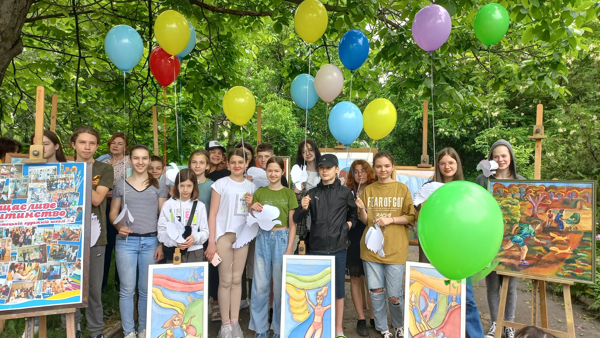 Група учнів з малюнками серед святкових кульок у дворі